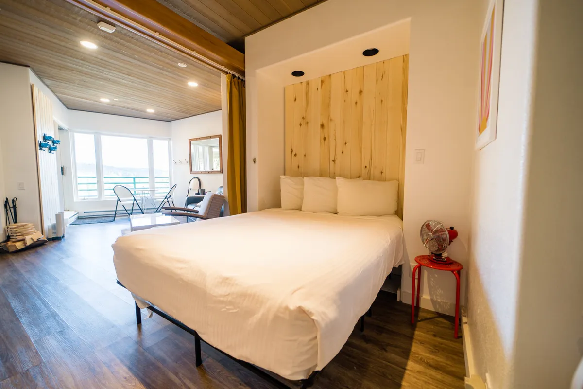 A peaceful bedroom scene with a plush bed, warm wooden walls, a cozy seating area, and expansive windows offering serene views. The space feels inviting and tranquil, perfect for restful evenings and mornings filled with natural light.