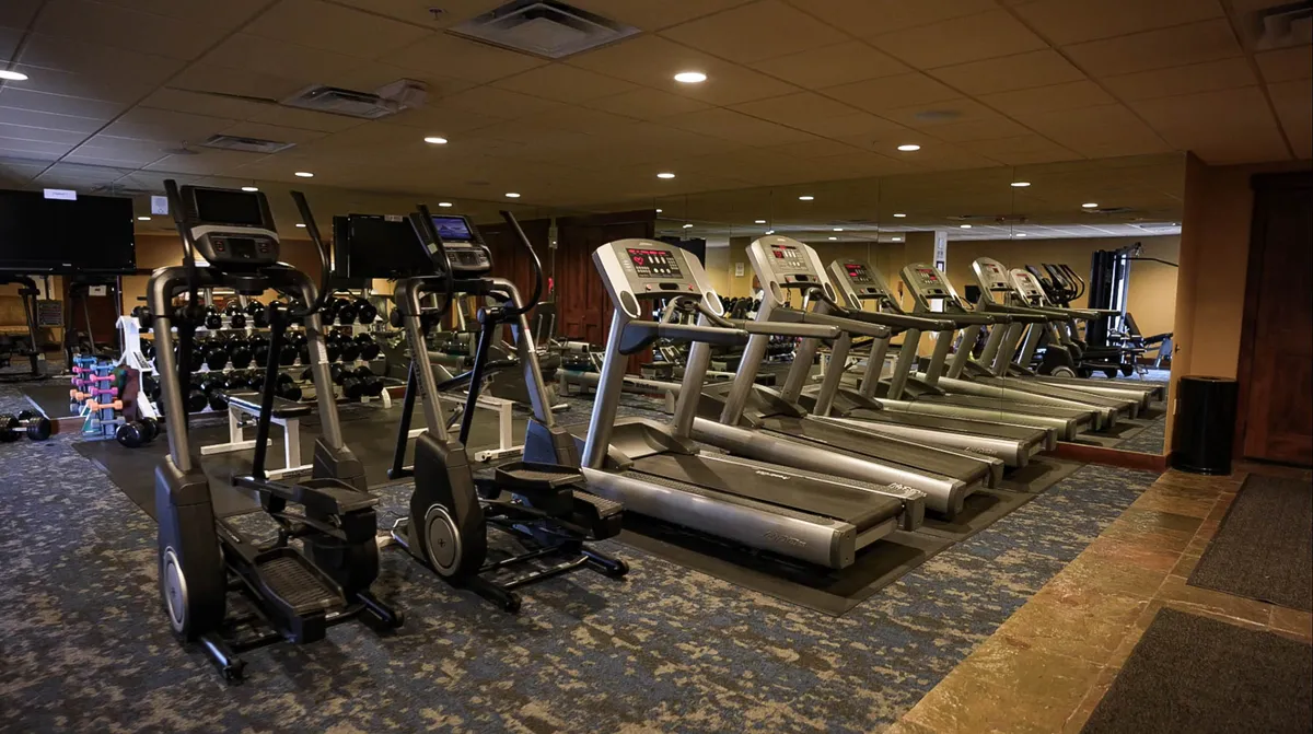 A modern, well-equipped exercise facility featuring treadmills, elliptical machines, dumbbells, and full-wall mirrors. The room exudes an invigorating atmosphere, making it ideal for cardio and strength training, group classes, or solo workouts.