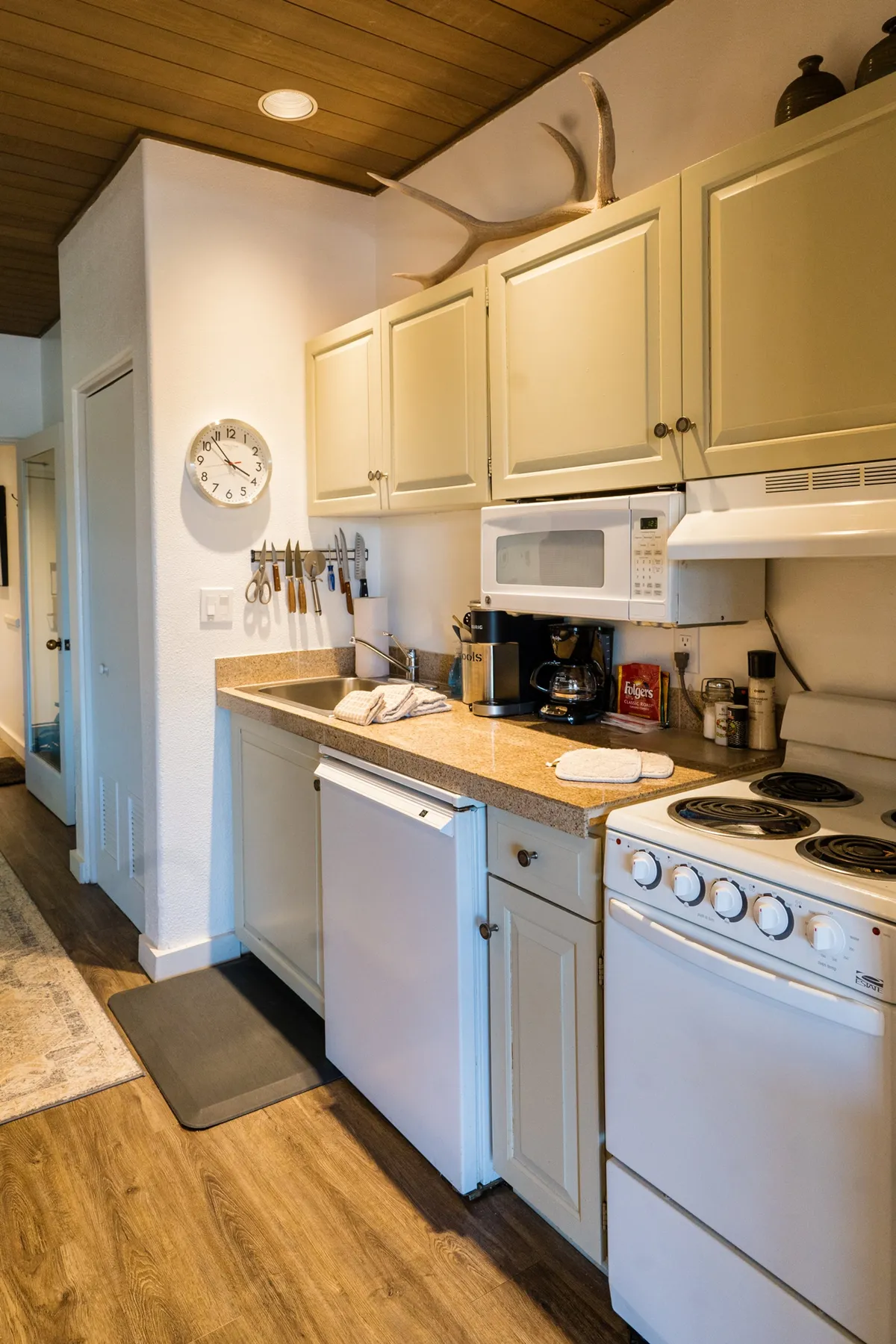 An inviting efficiency kitchen with wooden cabinets, a stove, sink, and coffee maker, accented by decorative touches like antlers. The space feels perfect for preparing quick meals or morning coffee in a home-like atmosphere.