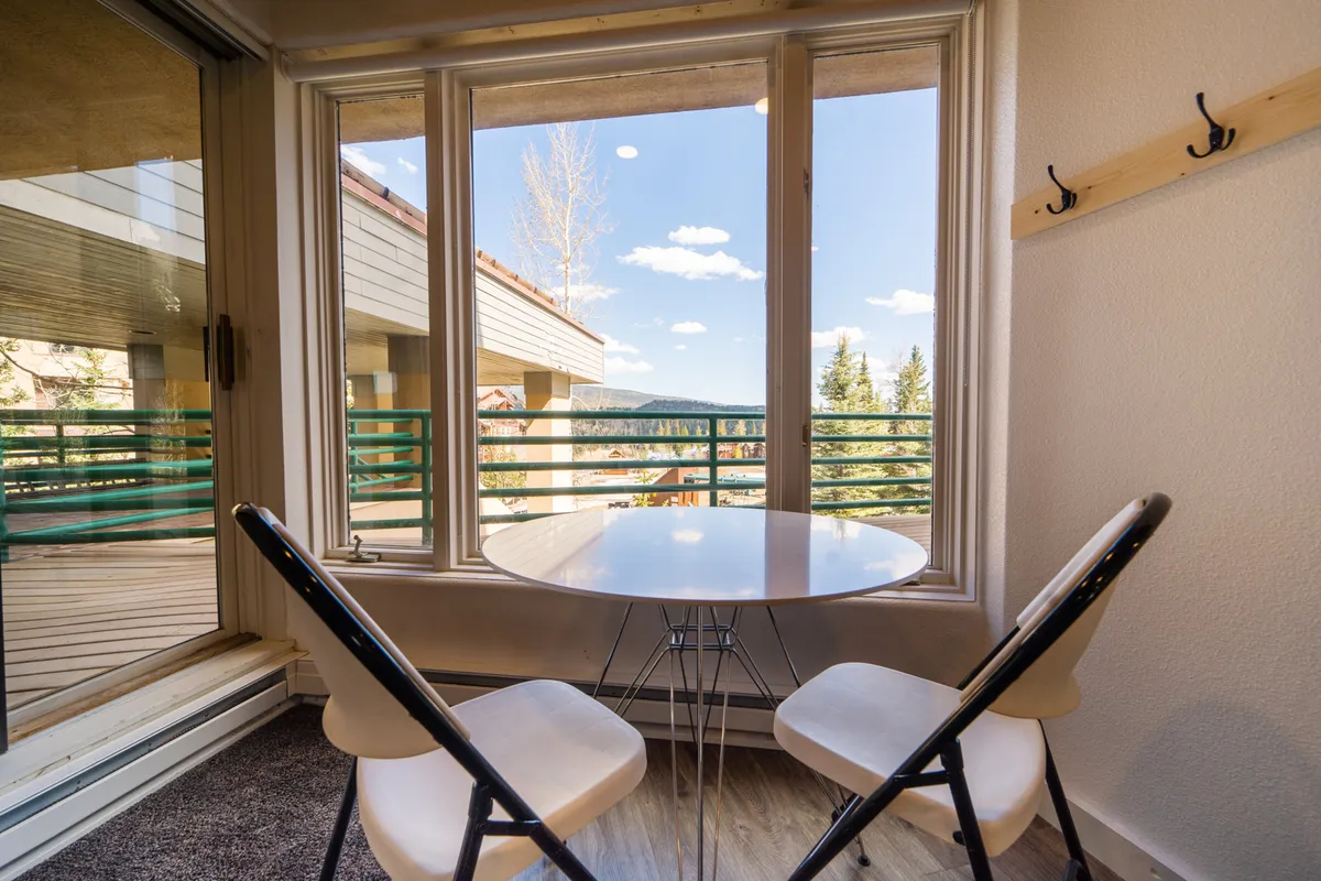 An inviting round table with two chairs is set beside a large window that frames a scenic view. Natural light fills the space, making it ideal for enjoying morning coffee or quiet moments while appreciating the outdoors from within.